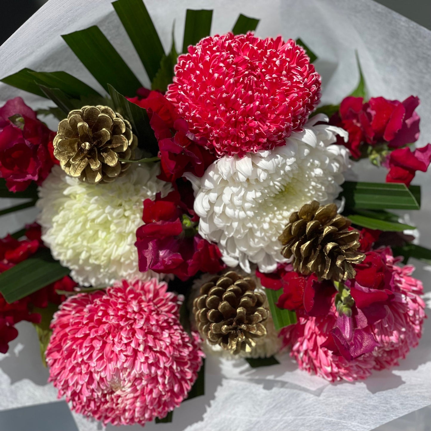 Bouquet of red and white flowers with gold pinecones on a white background